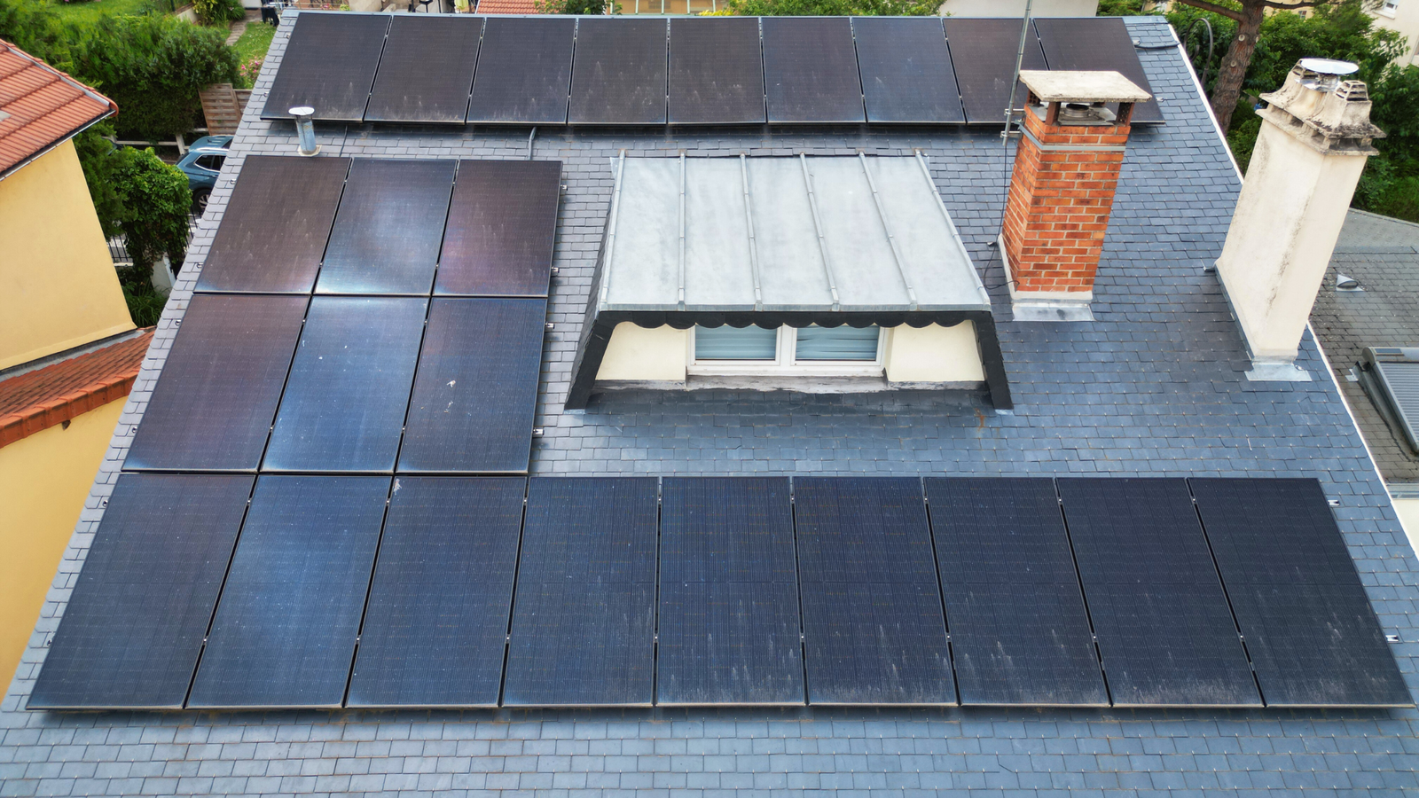 Vue rapprochée d'un toit de maison avec des panneaux solaires, une lucarne et une cheminée en briques.